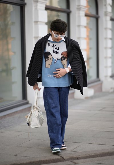 Suéter de punto con estampados de dibujos animados, azul y beige. Blazer a rayas negra, jeans azules y un bolso blanco. Zapatillas con detalles en verde y rosa.