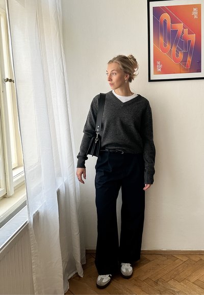 Jersey de punto gris oscuro con escote en V, usado sobre una camiseta blanca, combinado con pantalones negros holgados. Accesorios con un bolso de hombro negro.