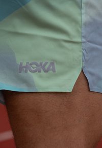 Lette shorts i pastell mintgrønn med abstrakte mønstre. Fremhevet "HOKA"-logo i grått, sideslitt for bedre bevegelighet.