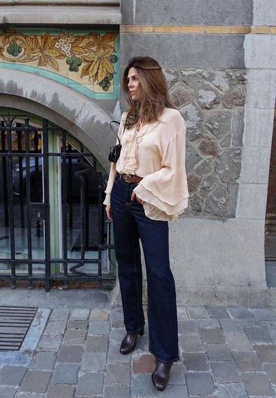 Blusa de melocotón claro, con volantes y mangas anchas, combinada con vaqueros acampanados de color azul oscuro y botas de tobillo marrones. Accesorio: bolso negro pequeño.