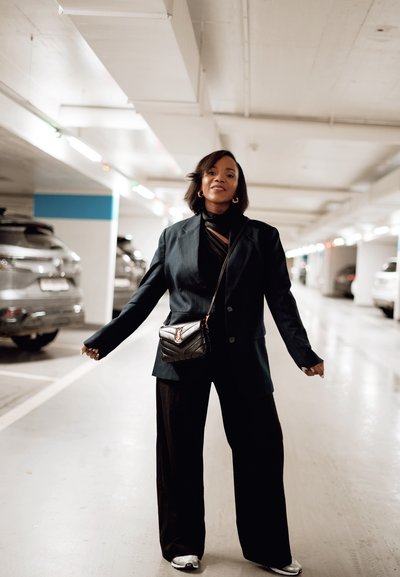 Blazer negro ajustado sobre una camiseta negra y pantalones de pierna ancha, combinado con zapatillas plateadas. Un pequeño bolso cruzado negro con un diseño acolchado.