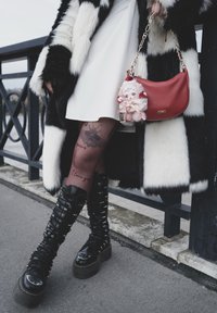 Svart-hvitt fuskepelsjakke, hvit kjole, rød veske med myk dukke, mønstrede svarte strømpebukser og høye svarte platåstøvler med sølvdetaljer.