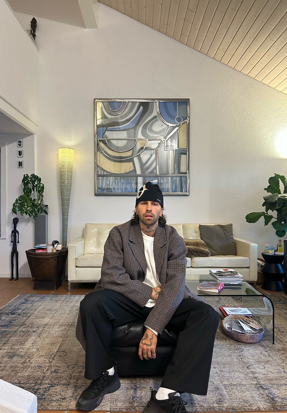 Moderne værelse med en hvid lædersofa, et mønstret tæppe, et glas sofabord og stor abstrakt vægkunst. Indeholder en høj, struktureret lampe og en plante.