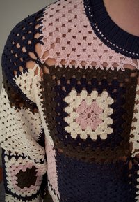 Suéter tejido a ganchillo con un diseño de patchwork en azul marino, rosa, crema y marrón. Textura notable con patrones de tejido abierto y motivos geométricos.