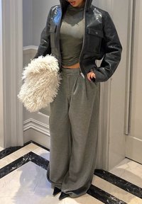 Sort læderjakke med hætte, grå tætsiddende top, grå sweatpants med vide ben og en fluffy hvid taske. Sorte remsandaler fuldender looket.