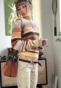 Pull en maille rayé marron, beige et bleu ; pantalon cargo taille haute beige ; sac marron clair avec des anses marron ; manches courtes ; tissu texturé.