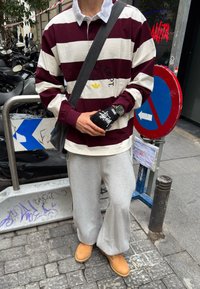 Maroon and white striped long-sleeved shirt over a white collared shirt, paired with grey joggers and tan clogs. Accessories include a black bag and a watch.