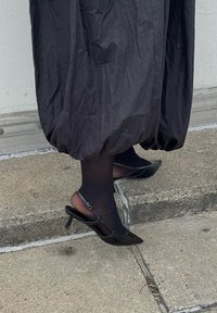 Fekete slingback magassarkú cipők hegyes orral, sima anyagból készült. Vékony boka pánttal rendelkezik, apró csattal.