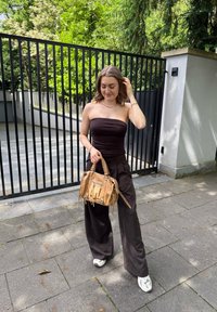 Svart strapless topp, mörka vida byxor och vita sneakers. Håller en beige handväska med flätad handtag och dragkedjedetalj.