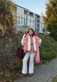 Felpa con cappuccio rosa chiaro con scritta "Colorado", giacca in pelliccia sintetica bianca, pantaloni grigi a zampa, sciarpa rosa, borsa a mano marrone e stivali marroni. Ambientazione naturale.