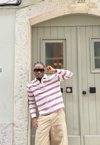 Chemise à manches longues blanche avec des rayures horizontales rouges et un col, assortie à un pantalon beige clair à jambes larges, devant un fond de porte neutre.