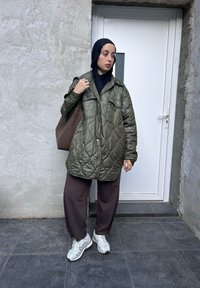 Καπιτονέ μπλε μπουφάν με κουκούλα, μαύρη μπλούζα, καφέ φαρδιά παντελόνια και λευκά αθλητικά παπούτσια. Περιλαμβάνει μια καφέ τσάντα ώμου.