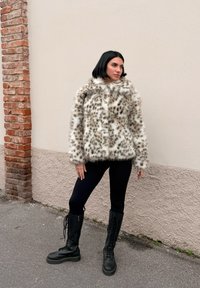 Leopard print faux fur jacket with a high collar, paired with black leggings and lace-up black combat boots against a neutral wall backdrop.