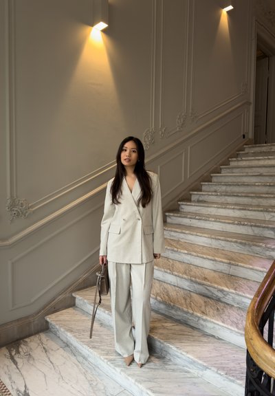 Traje gris claro hecho de tejido entrelazado, con un blazer de doble botonadura y pantalones de pierna ancha. Combinado con un bolso pequeño marrón y tacones beige.