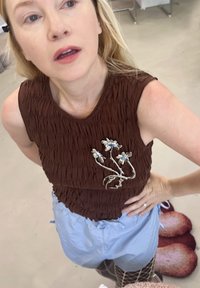 Top fără mâneci, texturat, de culoare marron, cu un broșă florală, asortat cu pantaloni scurți de un albastru deschis, dotati cu șnururi de strângere, și ciorapi cu plasă modelată.