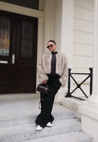 Ψεύτικη γούνα μπεζ cropped τζάκετ, μαύρος λαιμός (turtleneck), φαρδιά μαύρα παντελόνια και λευκά sneakers. Καφέ τσάντα με χρυσή λεπτομέρεια στο φερμουάρ.