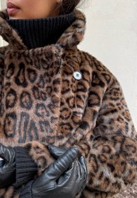 Manteau en fausse fourrure à imprimé léopard avec un col roulé côtelé noir, orné d'un bouton noir et accompagné de gants en cuir noirs. Texture douce et coupe ample.