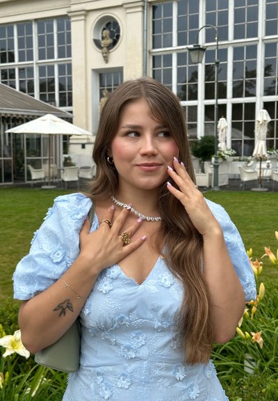 Vestido bordado de color azul claro con mangas abullonadas, escote en forma de corazón, adornado con un collar brillante y anillos de oro.