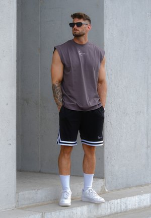 Camiseta de algodón sin mangas de color púrpura oscuro con logo blanco; pantalones cortos negros con franjas blancas; zapatillas blancas; ropa atlética casual de color sólido.