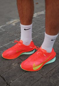 Chaussures de course roses néon vif avec des accents jaunes, en matériau mesh, au design épuré. Portées avec des chaussettes blanches Nike.