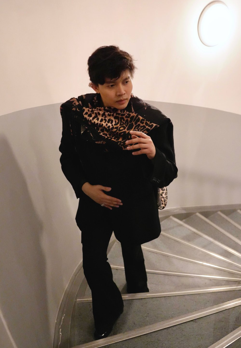 Blazer noir sur une écharpe à imprimé léopard, associé à un pantalon noir. Escalier en colimaçon visible en arrière-plan.