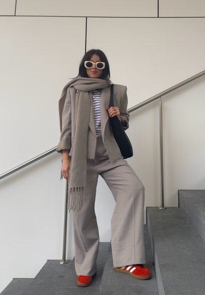 Traje ajustado gris claro con pantalones de pierna ancha, superpuesto a una camisa de rayas blanca y azul marino. Acabado con una bufanda gris y zapatillas rojas.