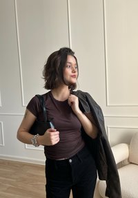 Barna, testhez simuló póló, fekete kordbársony nadrág, egy kis fekete kézitáskával a kezében. Egy fekete bőrdzseki a vállára terítve, beltérben.