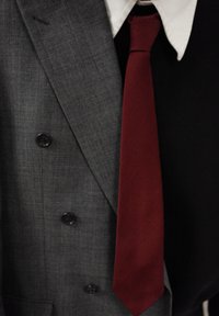 Veste de costume à carreaux gris avec boutons noirs, col de chemise blanc et cravate rouge. Les textures visibles comprennent une finition de tissu lisse.