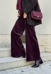 Burgundy corduroy levepöks, kombinert med en teksturert mørkebrun kåpe og en bordeaux veske. Klumpete ankelsko med hæl fullfører antrekket.