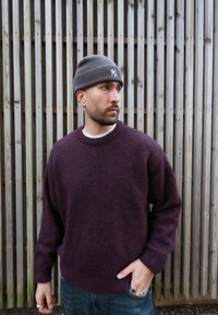 Pull en tricot prune avec poignets côtelés, col rond et coupe décontractée, associé à un bonnet gris en tricot avec un logo brodé.