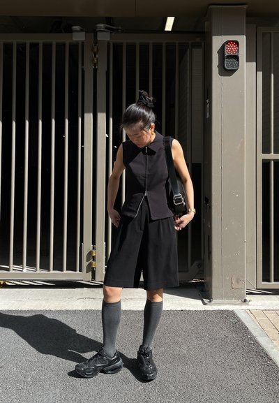 Top negro sin mangas con cremallera frontal, combinado con culottes negros. Medias altas de rodilla grises y zapatillas negras completan el look.
