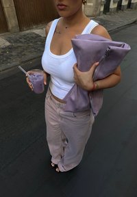 Osoba u bijeloj majici bez rukava i svijetloružičastim hlačama drži veliki ljubičasti clutch i šalicu s ledenim ljubičastim napitkom na ulici.