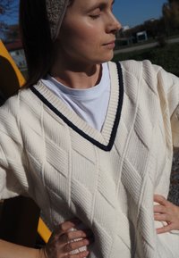 Cream-colored knitted sweater with a v-neck, featuring a navy blue trim and diamond textured pattern. Worn over a white t-shirt.