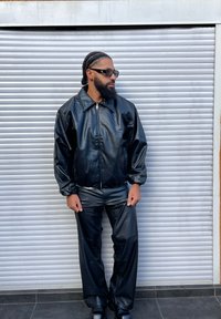 Czarna skórzana kurtka z zamkiem z przodu, zestawiona z czarnymi skórzanymi spodniami. Kurtka ma duży kołnierz i elastyczne mankiety dla luźnego dopasowania.