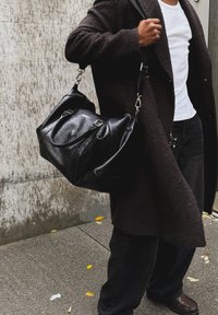 Black leather tote bag with curved design, dual top handles, detachable shoulder strap, and visible water droplets on the surface.