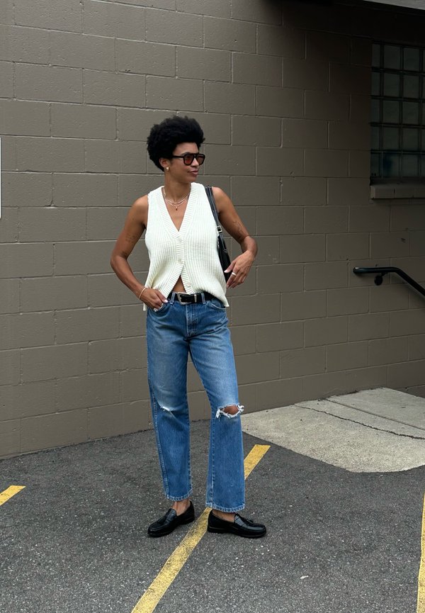 Vest crem cu dungi, blugi evazați cu talie înaltă și genunchi distruși, și loafers negri. Accesoriile includ coliere suprapuse și o poșetă.