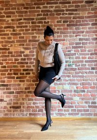 Umělá kožešinová vesta, žebrovaný dlouhý rukáv, černé šortky, průhledné černé punčocháče a černé lodičky. Pozadí červené cihlové zdi.