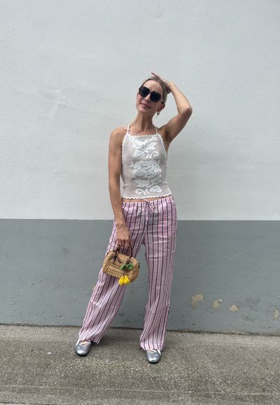 Top corto de encaje blanco con dobladillo con volantes, pantalones de pierna ancha a rayas rosas, zapatos plateados y un pequeño bolso de mimbre con acentos de frutas.