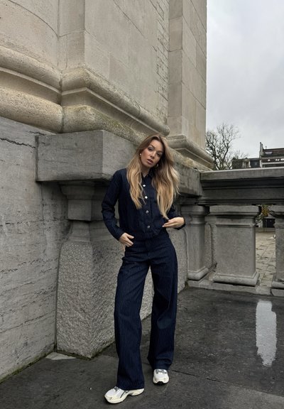 Conjunto de dos piezas a rayas azul marino hecho de tela texturada, que incluye una chaqueta con botones y pantalones acampanados, combinados con zapatillas de color claro.