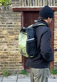 Mochila à prova d'água verde e preta com alças ajustáveis, fecho superior em rolha, bolso lateral e detalhes refletivos. Feita de material durável.