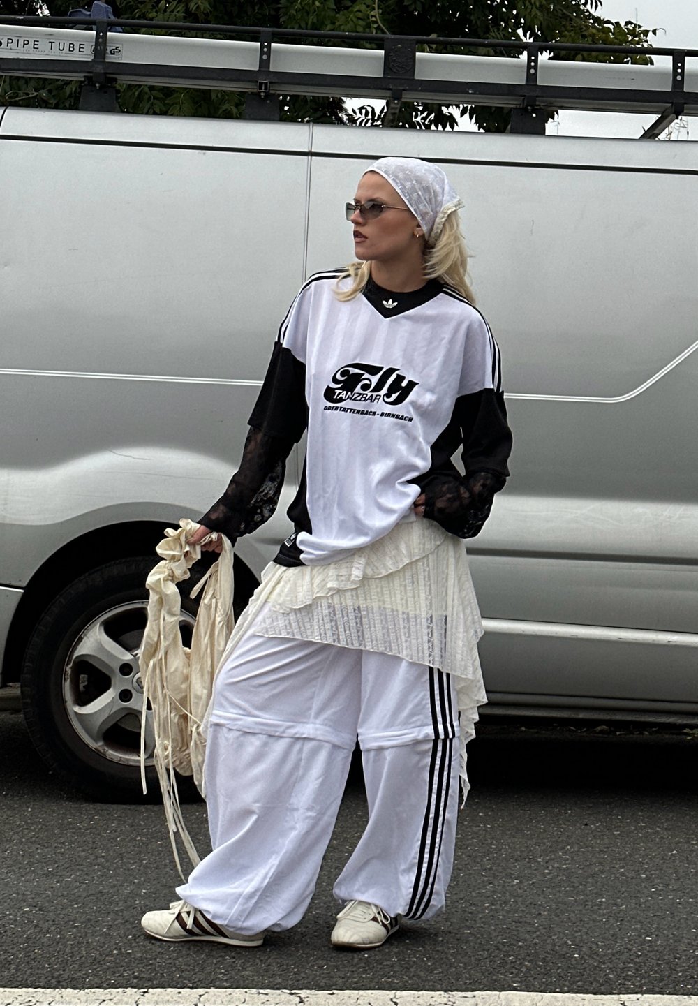 Oversized svart-hvitt sportskjorte med logo, lagdelt hvit skjørt, løse hvite bukser med svarte striper, og hvite sko. Tilbehør inkluderer et hodebånd og solbriller.
