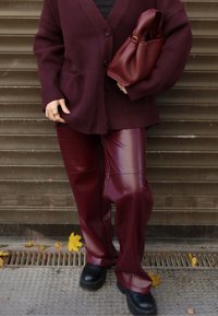 Bordó, bő fazonú gyapjú kardigán gombokkal, fényes bordó műbőr nadrággal és fekete platform cipővel párosítva, kezében hozzáillő táskával.