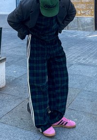 Grøn rutete seler med hvite striper, kombinert med en grå blazer og rosa joggesko, mot en bakgrunn av steinbelagte fortau.
