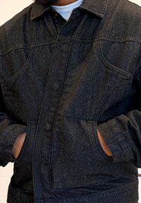 Veste en denim foncé à coupe ajustée, dotée de deux poches avant, de coutures visibles et d'un col classique. Tissu texturé avec peu de brillance.