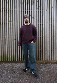 Pull bordeaux à col rond, jean bleu clair et chaussures noires avec des accents blancs, sur fond de lattes en bois.