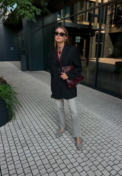 Blazer oversized negro, pantalones acampanados grises, zapatos de rayas de cebra y un bolso burdeos texturizado. Gafas de sol y un collar choker como accesorios.