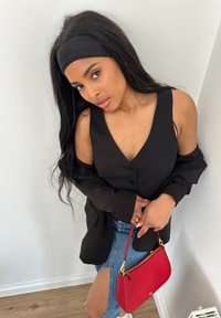 Sort knap-version uden ærmer, denimnederdel med slids, holder en rød håndtaske med guldbeslag. Langt sort hår og hovedbånd.