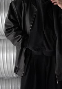 Svart skinnbomberjacka lager-på-lager över en svart huva-tröja, med en smal passform, kort längd och dragkedjedetalj.