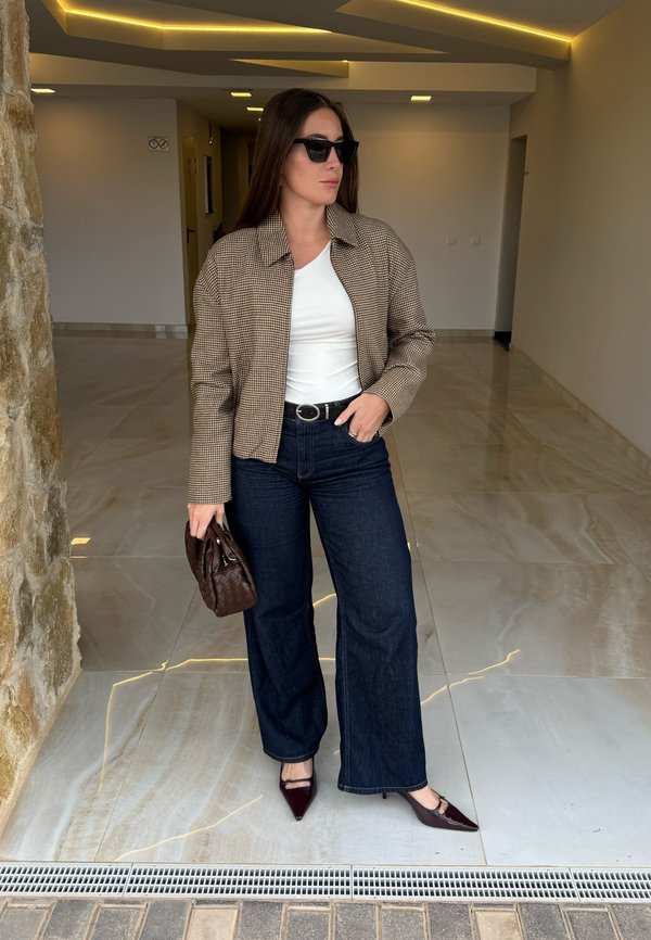 Bruine geruite cropped jas, wit overhemd, donkeren denim flared broek, zwarte zonnebril, bruine gevlochten handtas en bordeauxrode puntige hakken.