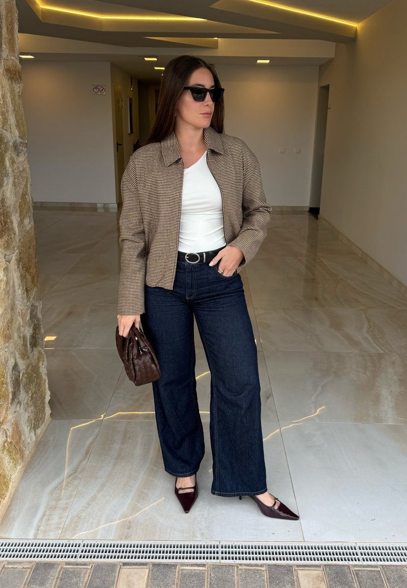 Brun rutete kort jakke, hvit skjorte, mørke denimvide bukser, svarte solbriller, brun vevd håndveske og burgunderrøde spisse hæler.